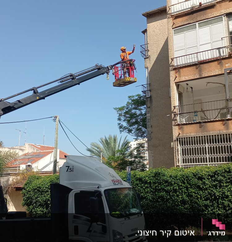 אדם במנוף עובד על איטום קיר בניין